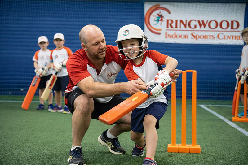 Coach helping a child learn cricket batting
